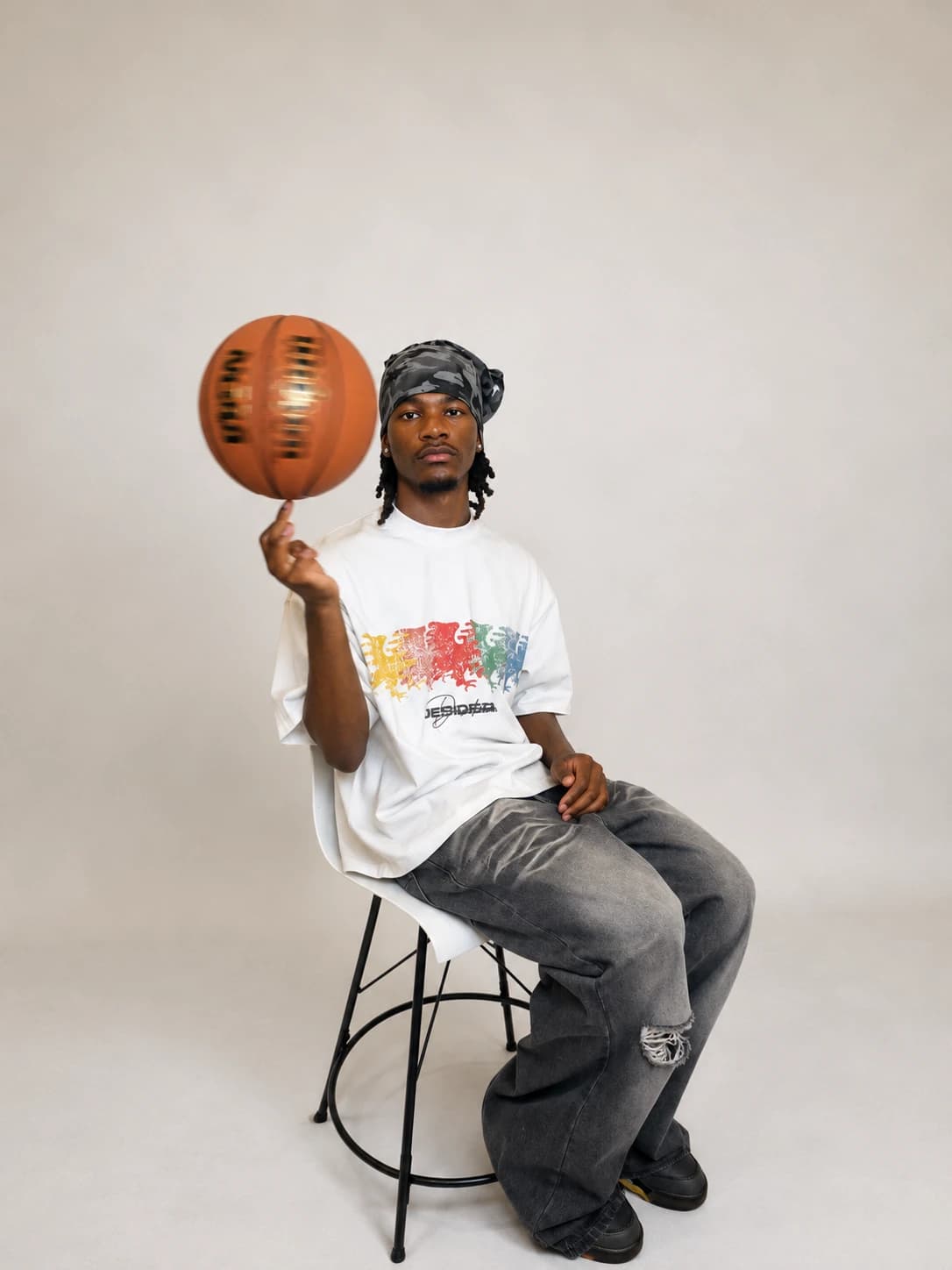 Seated on a stool in the multicolor eagle tee, spinning a basketball on one finger
